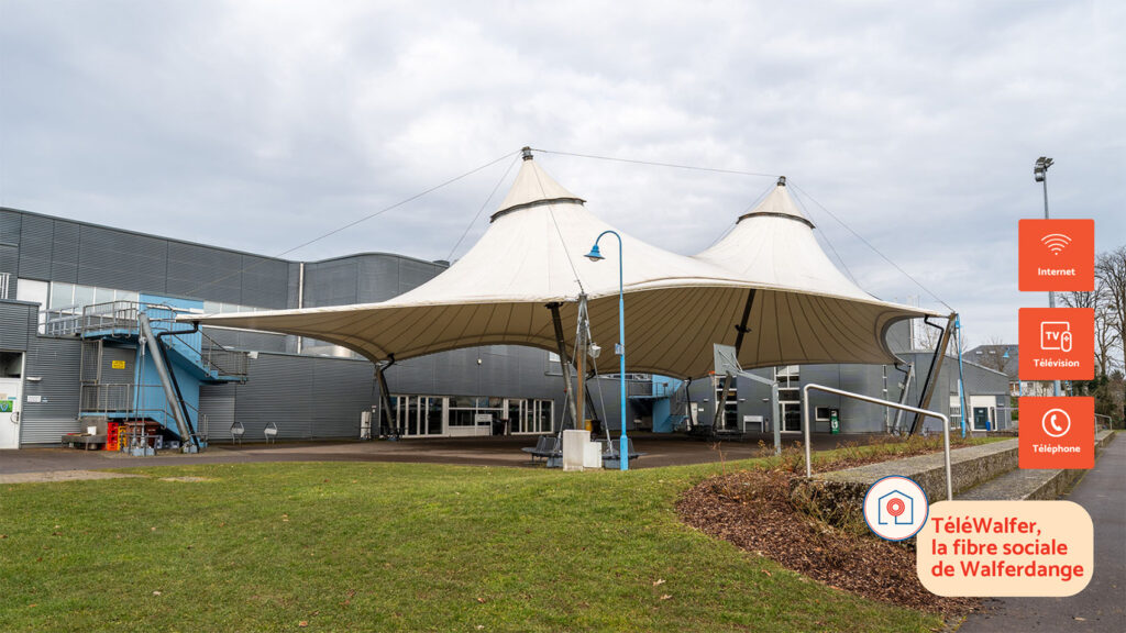 Exterior view of the Walferdange sports complex featuring a large white canopy structure. On the right, icons highlight Internet, TV, and Telephone services, with the slogan ‘TéléWalfer, la fibre sociale de Walferdange.