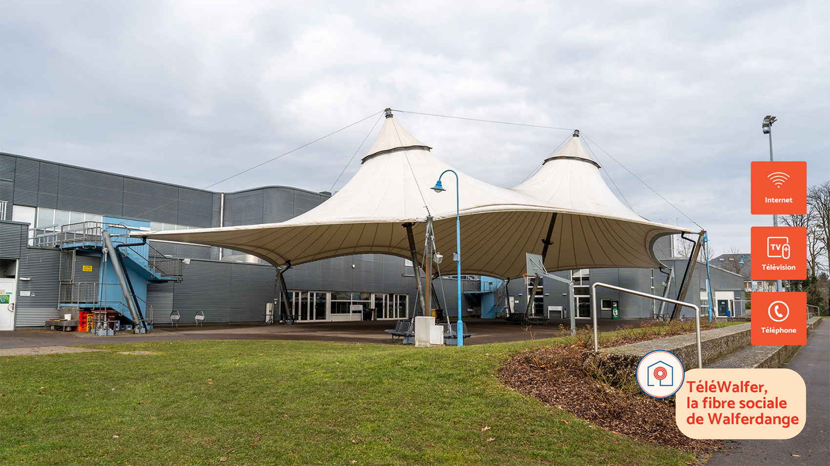Exterior view of the Walferdange sports complex featuring a large white canopy structure. On the right, icons highlight Internet, TV, and Telephone services, with the slogan ‘TéléWalfer, la fibre sociale de Walferdange.